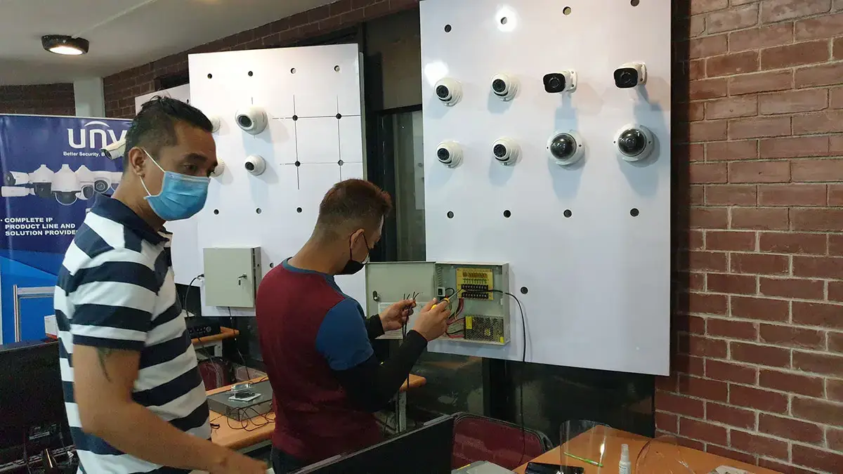 Hands-on CCTV training course in the Philippines showing students wiring a security surveillance system on a technical demonstration board.