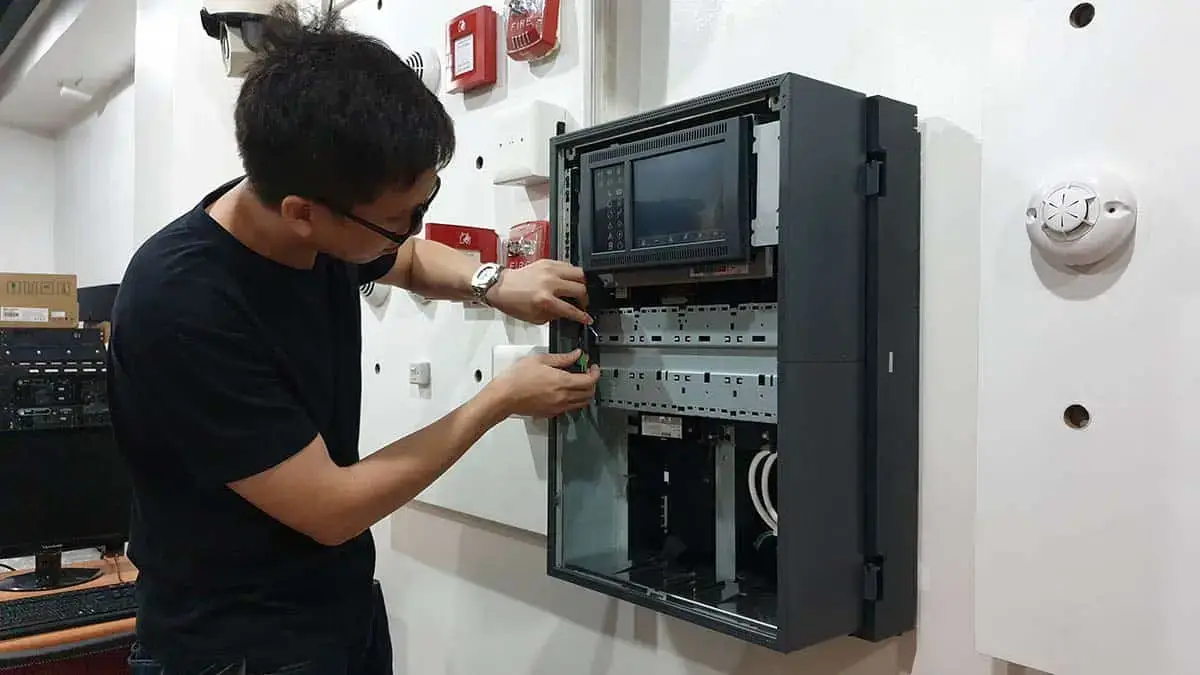 A student in the Philippines practicing the installation and wiring of a digital fire alarm control panel during an FDAS training session.