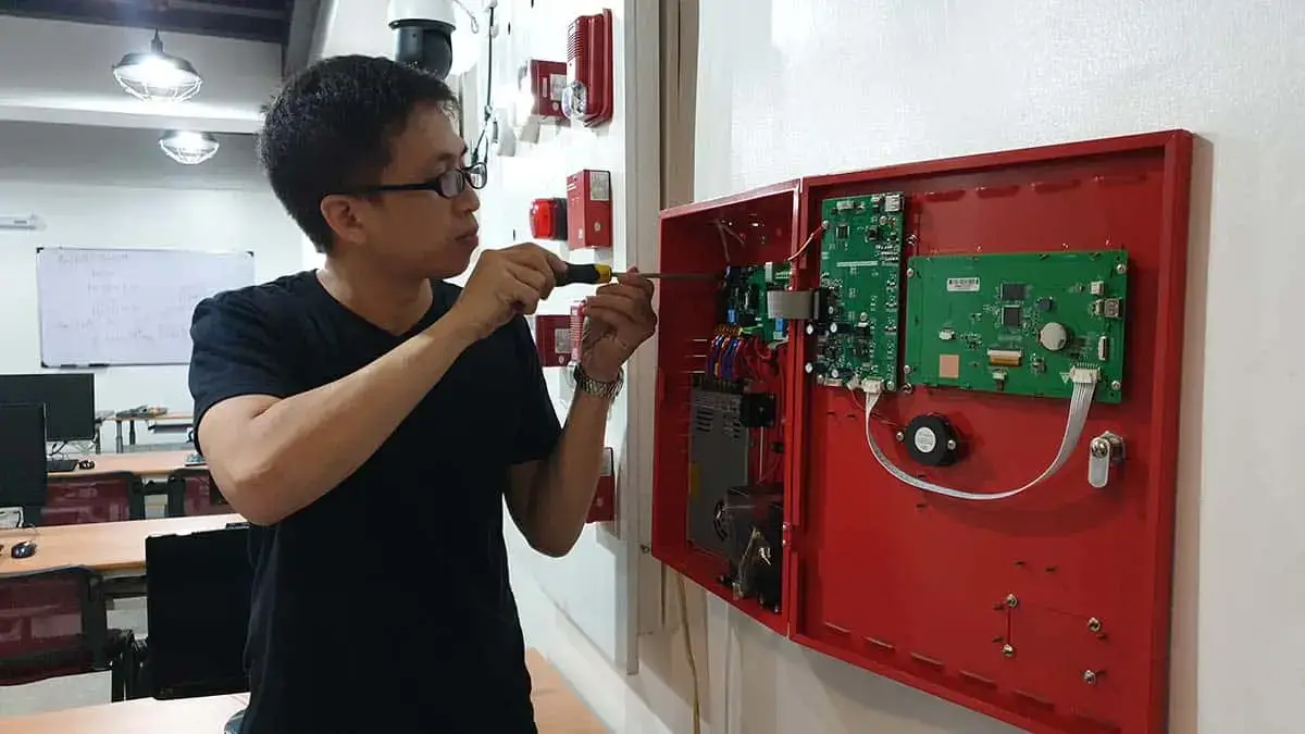 A technical student at a training center in the Philippines using a screwdriver to wire a fire alarm control panel during an FDAS course.