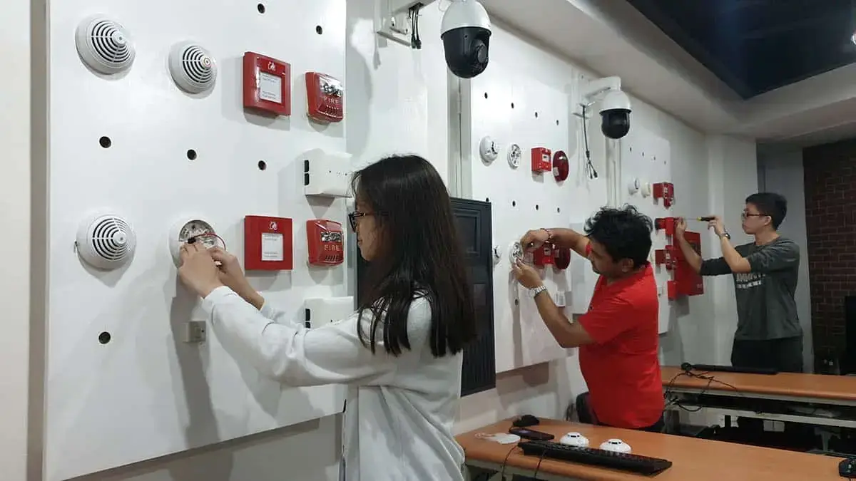 Students practicing fire detector installation on a training board during an FDAS training course in the Philippines