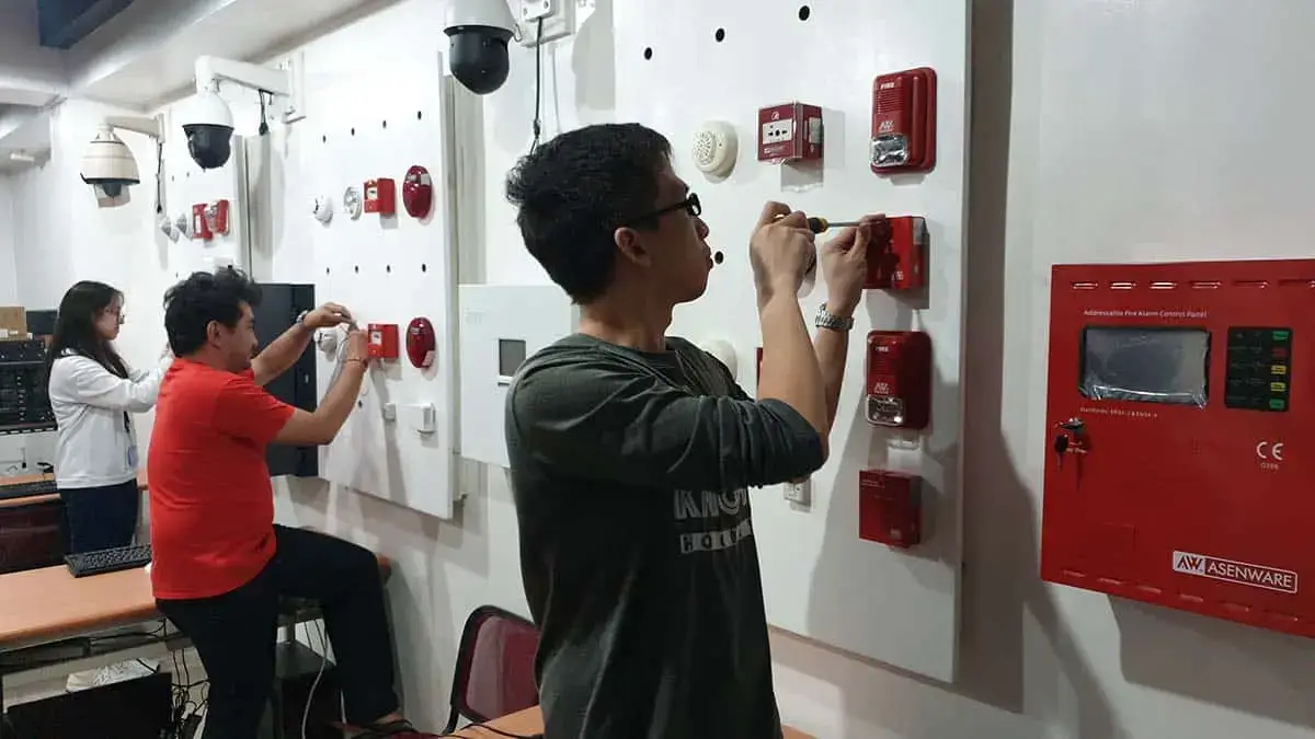 Students at a training center in the Philippines practicing the installation and maintenance of fire alarm systems on technical demonstration boards.