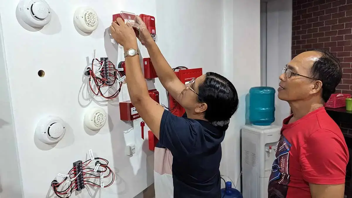Close-up of trainees working on FDAS wiring connections under the supervision of an expert