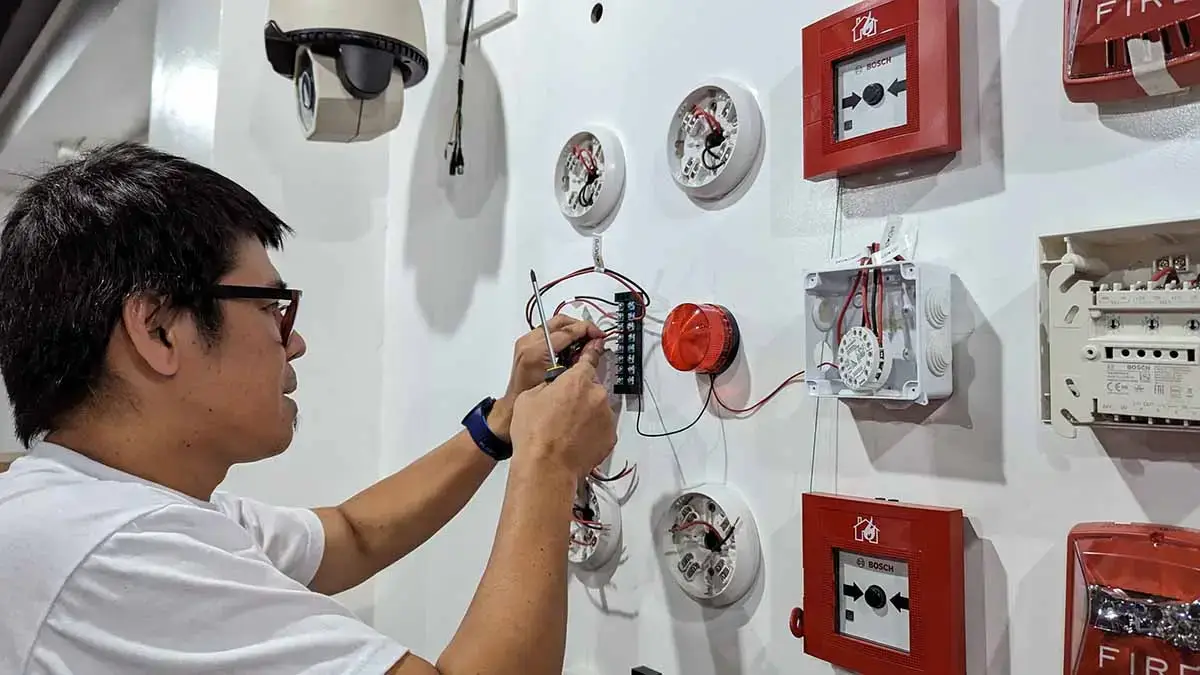 A technician performing hands-on wiring of a Bosch Fire Detection and Alarm System (FDAS) during a training course in the Philippines.
